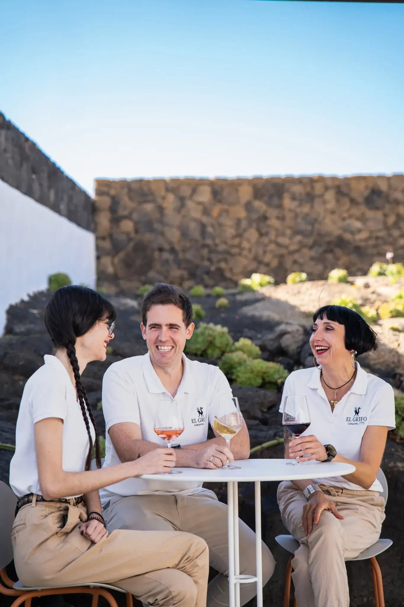 Equipo de enoturismo de la bodega, compartiendo una cata de vinos al aire libre entre viñedos volcánicos, con un ambiente distendido y sonriente.