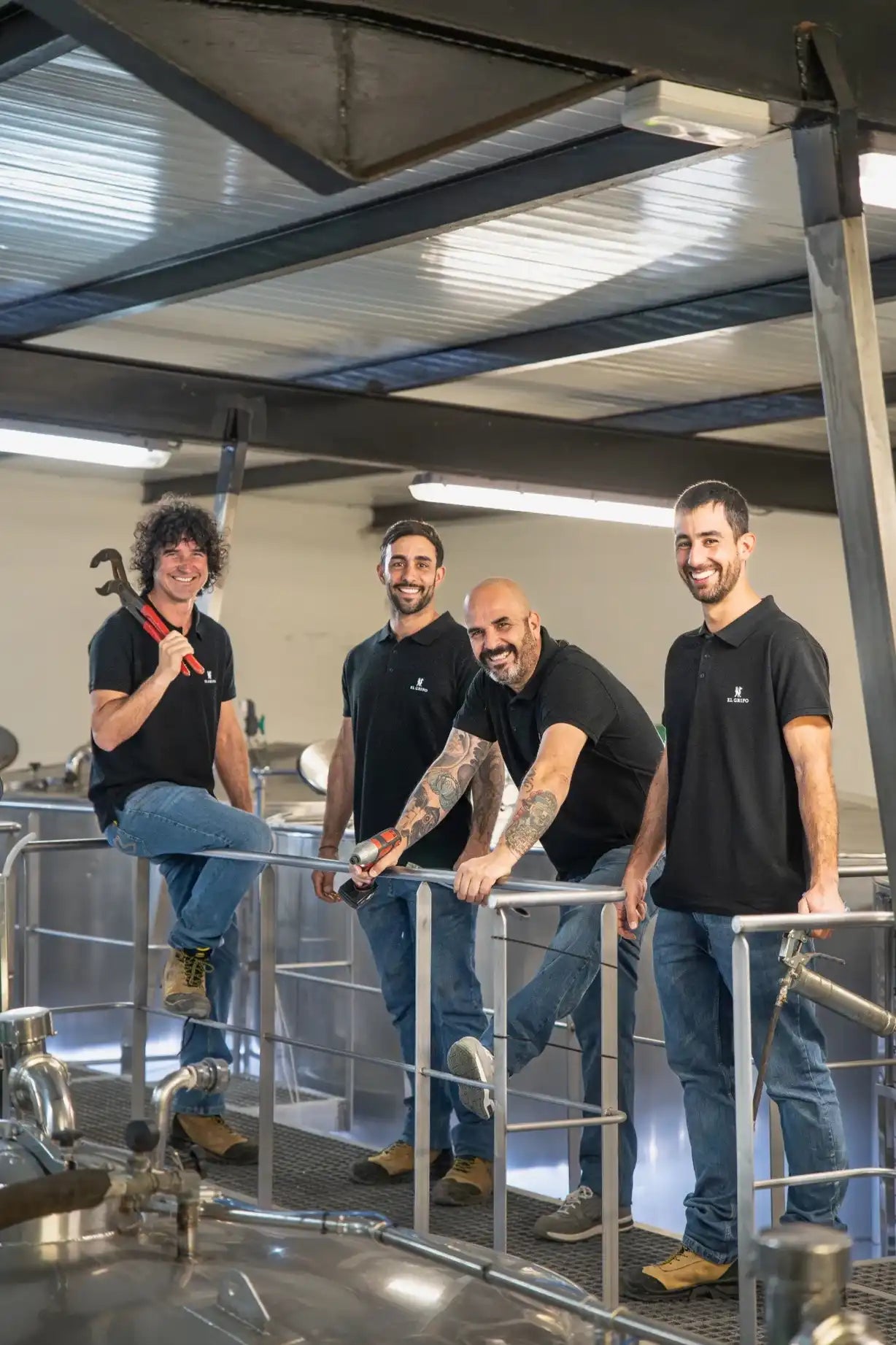 Equipo de mantenimiento de Bodegas El Grifo posando con herramientas sobre la pasarela metálica en la zona de depósitos, reflejando profesionalidad y buen ambiente laboral.
